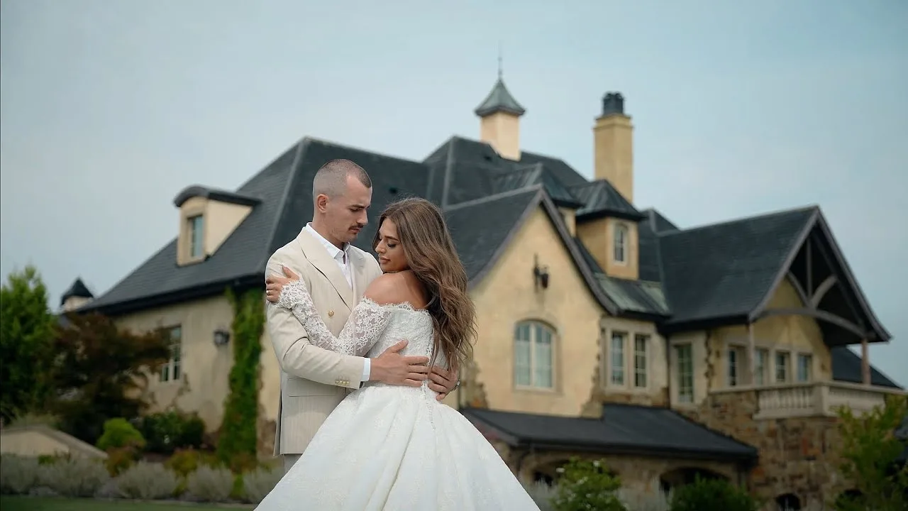 Groom in an ivory tuxedo embracing his bride in front of a stone chateau