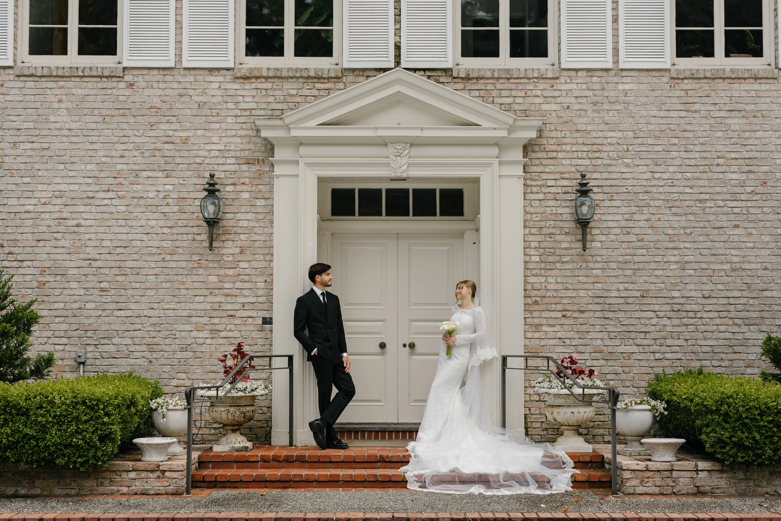Bride and groom smiling at each other on the steps of a brick manor with white double doors