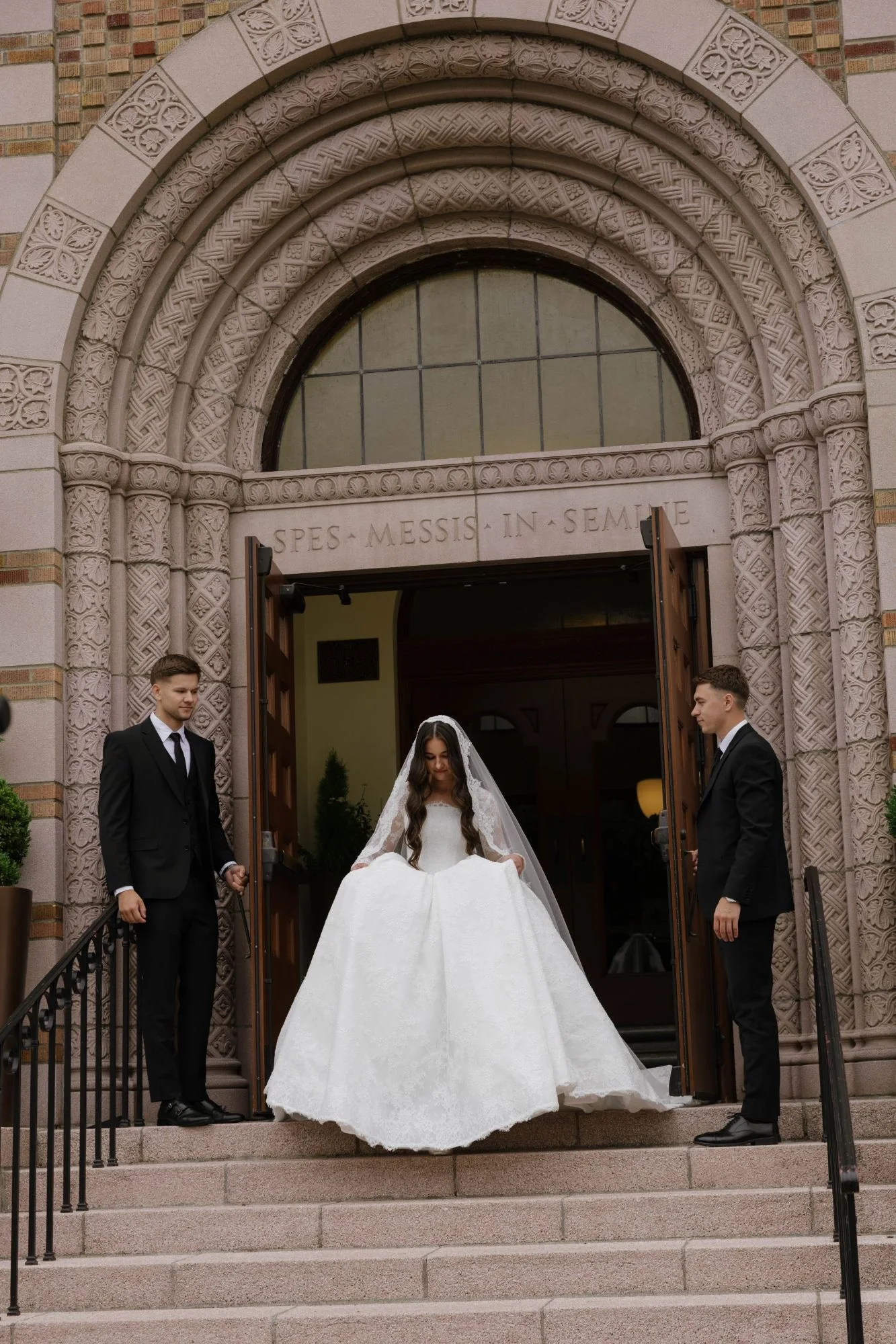 Bride stepping out of carved church doors as two groomsmen hold them open