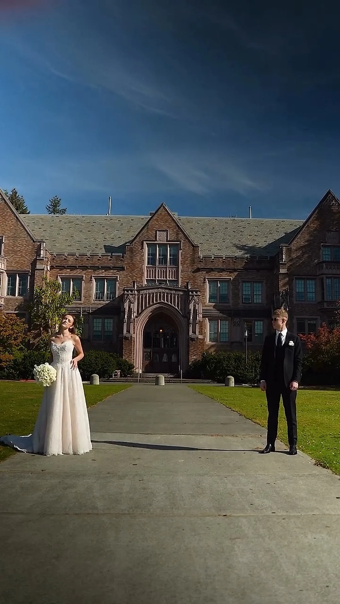 Bride and groom standing apart on a lawn before a brick manor
