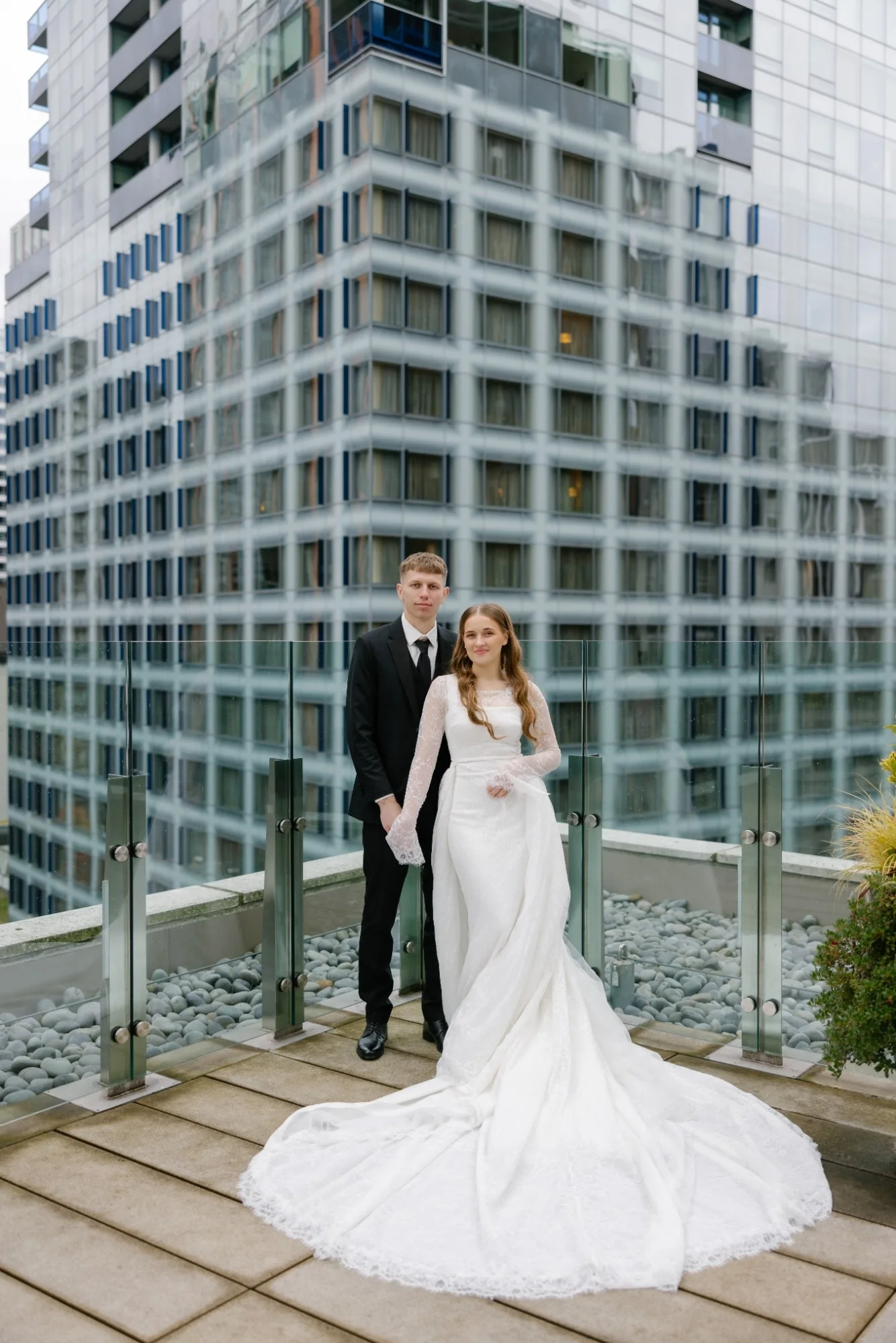 Bride with a long lace train beside the groom on a city rooftop terrace